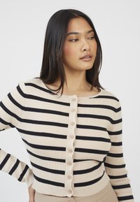 Beżowy i czarny sweter w paski, fabric ribbed, okrągły dekolt, zapięcie na guziki z przodu z ośmioma okrągłymi guzikami, dopasowany krój.