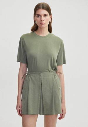 T-shirt vert olive à manches courtes avec un col rond, associé à un short taille haute avec des plis et des poches latérales, le tout dans une teinte assortie.