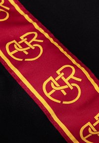 Sfondo di tessuto nero con un nastro rosso caratterizzato da un motivo di logo giallo ripetuto, bordato da un sottile bordo giallo.