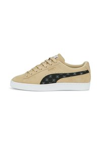 Beige semišové tenisky s texturovaným černým logem Puma, bílé gumové podrážky a odpovídajícími tkaničkami. Obsahují jemné vzorované detaily na logu.