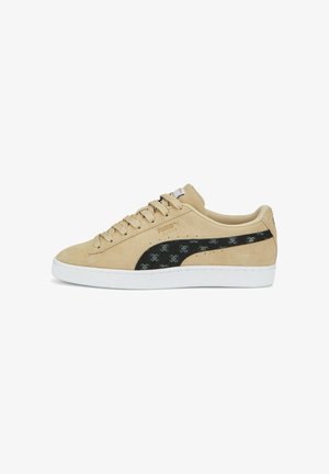 Beżowe zamszowe sneakersy z czarnym teksturowanym logo Puma, białą gumową podeszwą i dopasowanymi sznurówkami. Zawierają subtelne wzorzyste akcenty na logo.