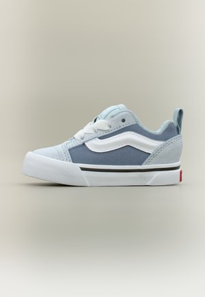 Baskets basses avec panneaux en daim bleu clair et tissu, bande ondulée blanche, semelle blanche texturée et lacets blancs.