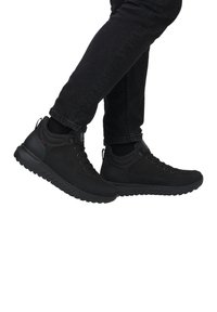 Chaussures de randonnée noires avec une tige synthétique texturée, des lacets ronds et une semelle en caoutchouc dotée d'un profil nervuré pour une meilleure adhérence. Portées avec un jean foncé.