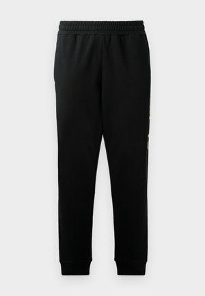 Black sweatpants with an elastic waistband, tapered legs, and side pockets. Features a bold graphic detail along the left side.