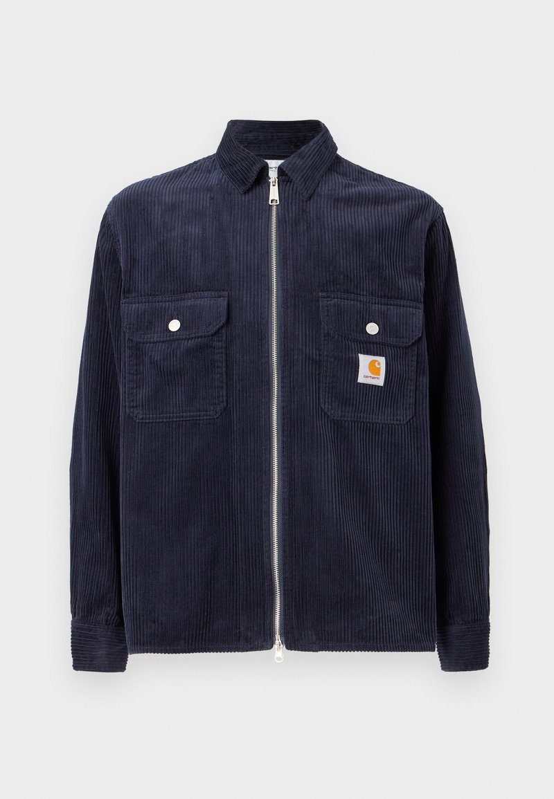 Marineblauwe corduroy jas met een rits aan de voorkant, twee borstzakken en geribbelde manchetten. Bevat een klein logopatch op de linkerzak.