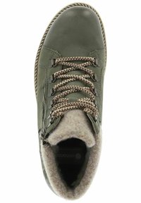 Botín de cuero verde con forro de lana marrón, cordones trenzados y cremallera lateral. Presenta una suela texturizada y costuras en contraste.