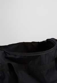 Borsa da viaggio in tela nera con chiusura a zip, manici robusti e una superficie liscia. L'interno è spazioso, progettato per un uso versatile.