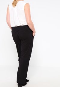 Svarta byxor med rak bendesign, tillverkade av ett glatt tyg, med sidofickor och midjeband, bärs med en vit ärmlös topp.