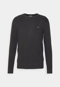 Černý pletený svetr s texturovaným vzorem, kulatým výstřihem a dlouhými rukávy. Malé logo na levé straně hrudi.