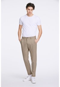 Pantaloni a righe marrone chiaro con una vestibilità slim, tasche frontali e chiusura con un solo bottone, abbinati a una maglietta bianca semplice e sneaker bianche.