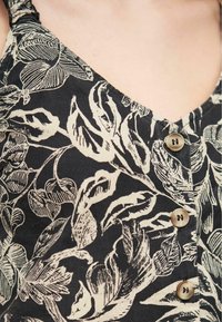 Top in tessuto nero a stampa floreale con scollatura a V, caratterizzato da motivi di foglie beige e quattro bottoni tondi beige lungo la parte frontale.