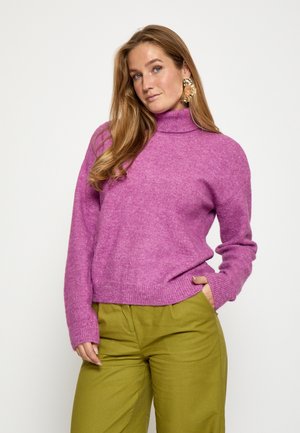 Magenta turtleneck sweater i blødt strikket stof med ribbede manchetter og kant. Parret med højtaljede olivengrønne bukser, der har sidelommer.