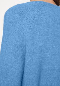 Maglione azzurro lavorato a maglia con una texture morbida, caratterizzato da un collo rotondo e un design con spalle scese. Costine visibili lungo la cucitura della spalla.