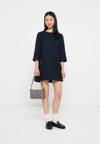 Marinekjole med tre kvarters klokkermerker, med to frontlommer med gullaksenter. Kombinert med en mønstret håndveske og svarte loafers.