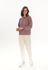 Paarse sweatshirt met geribde manchetten, gecombineerd met crèmekleurige, taps toelopende broeken en witte sneakers. De stof lijkt zacht en heeft een ontspannen pasvorm.