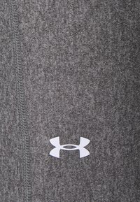 Grå träningsleggings i tyg med ett texturerat mönster, med en vit Under Armour-logotyp på vänster sida. Sömmar är synliga.