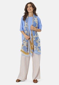 Light blue T-shirt, patterned blue and tan scarf, striped wide-leg pants in light colors, and brown sandals. Smooth fabric texture.