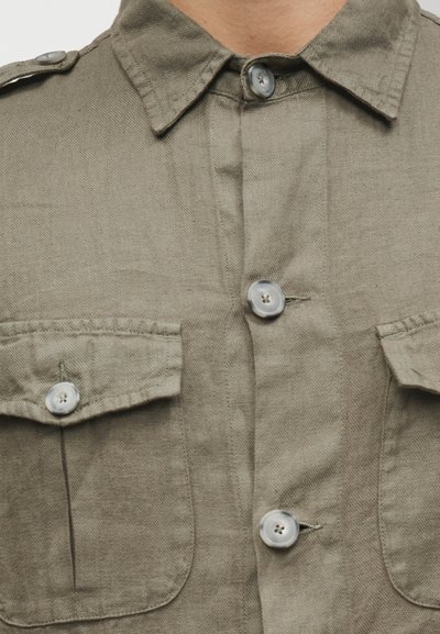 Πουκάμισο σε ελιά πράσινο χρώμα με κουμπιά στο μπροστινό μέρος, δύο τσέπες στο στήθος και κλείσιμο με κουμπιά. Κατασκευασμένο από υφή υφάσματος, με κλασικό γιακά.