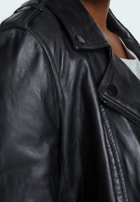 Zwarte leren motorjack met een soepele textuur, epauletten op de schouders en een ritssluiting aan de voorkant, met drukknopen.