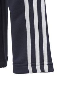 Pantalones deportivos azul marino con tres rayas verticales blancas a lo largo de los lados, hechos de una tela suave con costuras cosidas en el dobladillo.