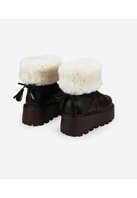 Botas de tobillo de cuero marrón con un puño de pelaje sintético blanco esponjoso, detalles de cordones y una suela de plataforma gruesa con un fondo texturizado.