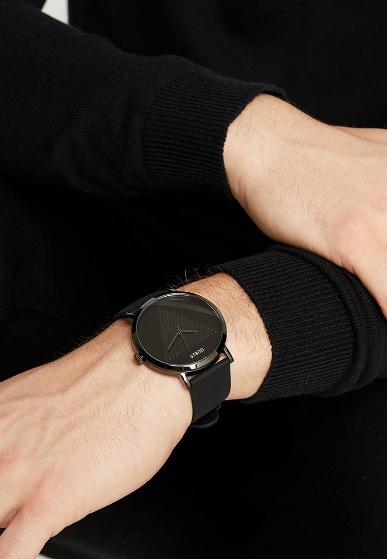 Ceas analog negru cu un cadran texturat negru și un model triunghiular; are o brățară elegantă din silicon negru și accente argintii.