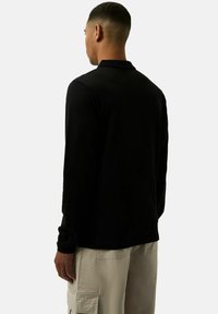 Czarna, długa koszulka polo z klasycznym kołnierzykiem, gładką fakturą i dopasowanym krojem, połączona z jasnobeżowymi spodniami cargo.