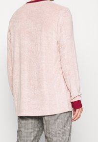 Långärmad, ljusrosa sweatshirt med en mjuk textur. Har en vinröd krage och subtila vertikala sömmar.