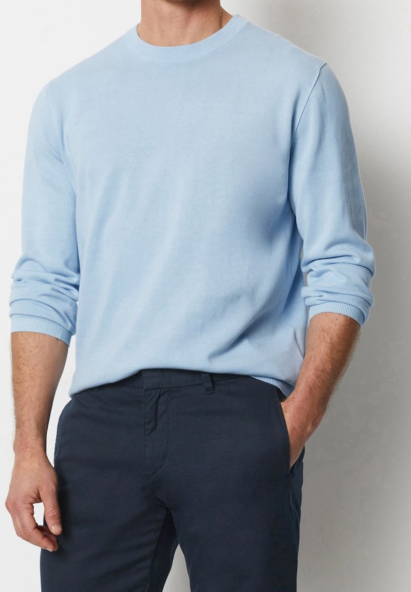 Maglione azzurro chiaro a collo rotondo realizzato in materiale morbido, con maniche lunghe e polsini a coste, abbinato a pantaloni blu navy.