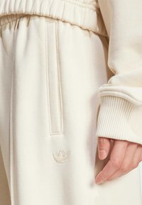 Pantaloni della tuta color crema con vita elastica, tasca laterale e polsini a costine. Presenta un piccolo logo ricamato sulla coscia.