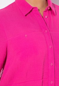 Fuchsia Hemd mit Knöpfen aus strukturiertem, gewebtem Stoff; verfügt über einen Kragen und zwei Brusttaschen, die mit runden Knöpfen verschlossen sind.