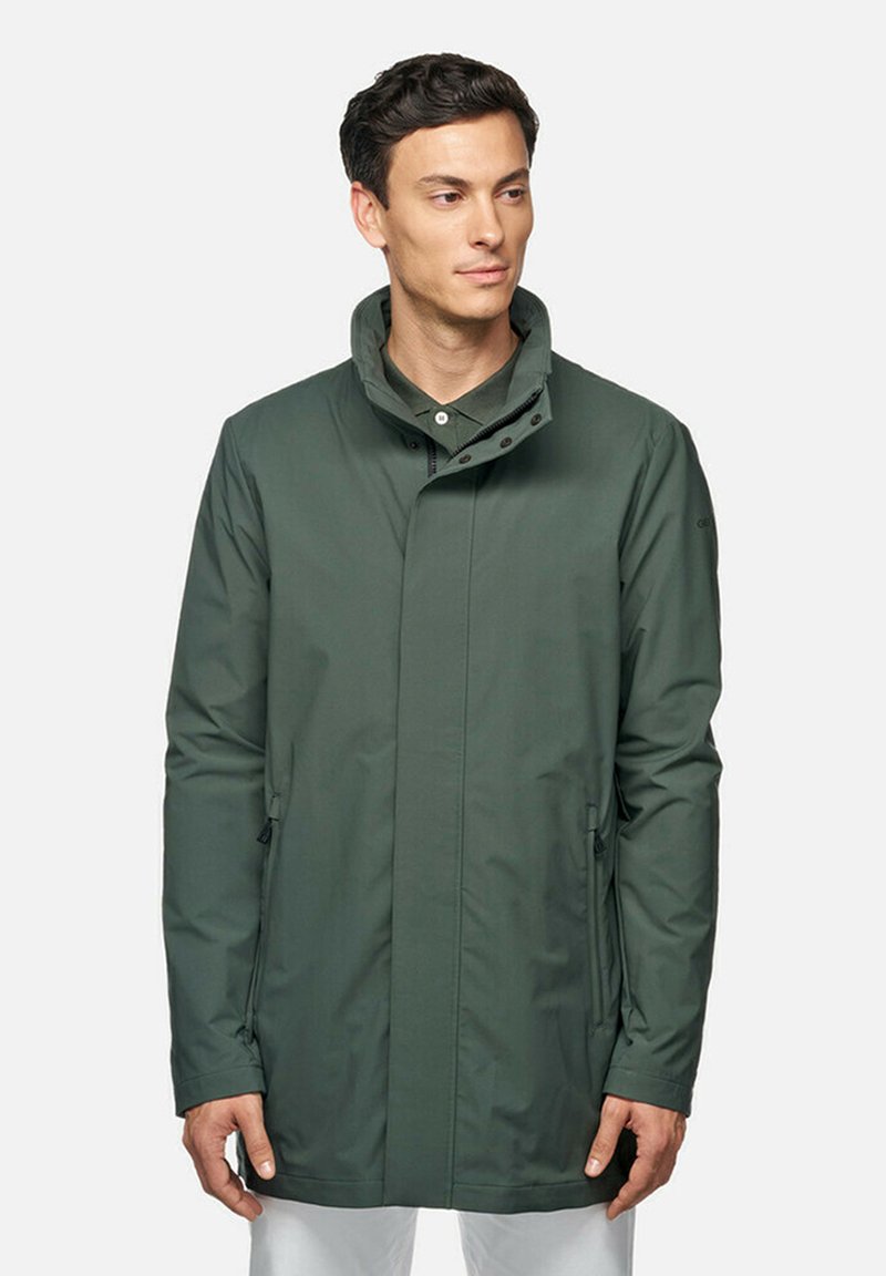 Giacca impermeabile verde scuro con colletto alto, tasche laterali e una texture liscia. Presenta una chiusura con zip e bottoni per un fissaggio sicuro.