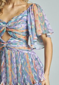 Bunt gefaltetes Kleid mit lila Grundfarbe, das geometrische Muster in Pastelltönen aufweist. Cut-out-Details in der Taille, kurze Flatterärmel.