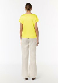 Żółta bluzka z krótkim rękawem o luźnym kroju, zestawiona z kremowymi spodniami z szerokimi nogawkami, zaprezentowana z tyłu. Prosty design z gładką teksturą.