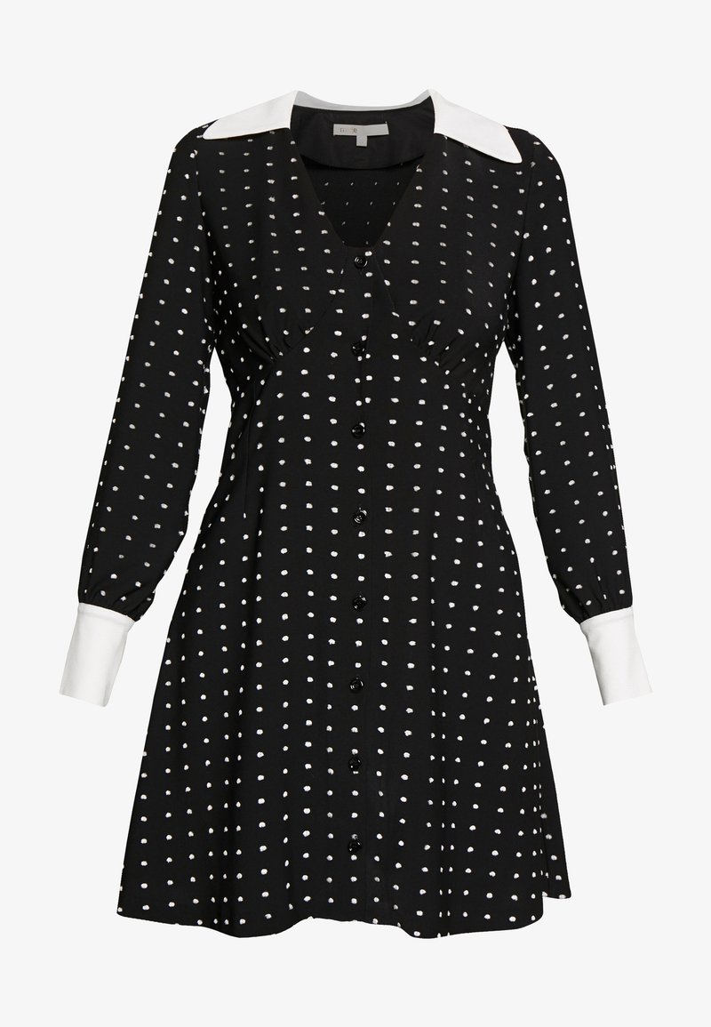 Robe noire à pois blancs, boutons sur le devant, col pointu blanc et poignets blancs aux manches longues.