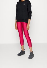 Black sweatshirt with a round neck, paired with shiny pink leggings featuring contrasting stitching, and black athletic shoes with textured design.