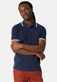 Granatowa koszulka polo z białym kołnierzykiem i akcentami na rękawach, krótki rękaw i prosty krój. Gładki materiał, minimalistyczny design.