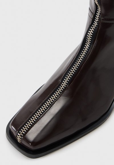Braune Lackleder-Ankle-Boots mit quadratischer Zehenform, ausgestattet mit einem sichtbaren Reißverschluss und einem kontrastierenden schwarzen Akzent an der Sohle.