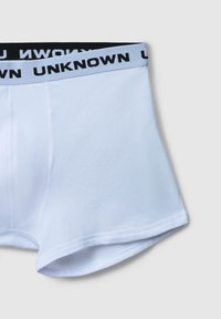 Białe szorty bokserskie z kontrastowym jasnoniebieskim paskiem w talii, na którym znajduje się czarny napis "UNKNOWN", przedstawione na jasnoszarym tle.