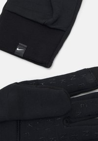 Black knit gloves featuring a textured palm with embossed lettering and a small Nike logo tag stitched on the cuff.