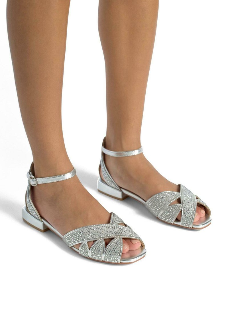 Zilveren sandalen met een open teen ontwerp, versierd met strassstenen en kruislings banden, met een lage blokhak en enkelbandje.