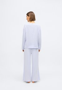 Svetlo modra komplet za sproščanje, ki vključuje dolg rokav in široke hlače. Mehka, gladka tkanina z udobnim krojem in minimalističnim dizajnom.