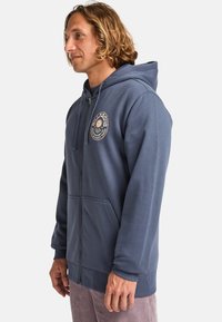 Felpa con zip color navy realizzata in tessuto morbido, con logo frontale, tasche a marsupio e polsini e orlo a coste.