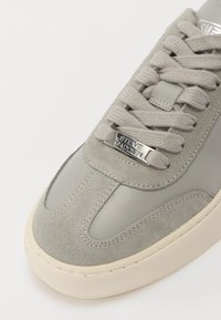 Sneaker gri dintr-un amestec de suede și materiale sintetice netede, vârf rotund, limbă căptușită și un detaliu cu logo argintiu. Talpă din cauciuc.