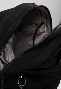 Bolsa negra con apertura con cremallera, forrada en una tela gris claro. Presenta un bolsillo interno con cremallera y un anillo de hardware plateado. Exterior texturizado.