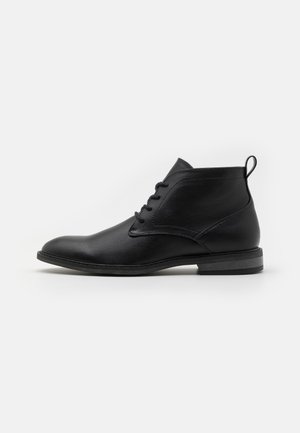 Botas de tornozelo em couro preto com bico arredondado, sistema de atacadores, pequena alça na parte de trás e acabamento texturizado na parte superior.