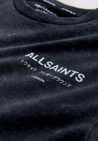 Musta AllSaints t-paita, jossa valkoista tekstiä sisältäen "ALLSAINTS", japanilaisia merkkejä ja "LONDON" edessä.