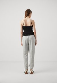 Svart tanktopp med tynne stropper kombinert med lysegrå joggebukser med elastiske mansjetter. Modellen vises fra baksiden.