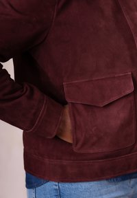 Burgundy suede jacket featuring a prominent front pocket, smooth texture, and ribbed cuffs, paired with blue denim.