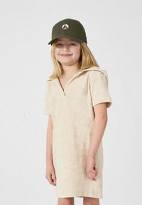 Vestido de algodón beige con cuello y mangas cortas, que presenta una textura sutil. El niño lleva una gorra de béisbol verde con un logo.